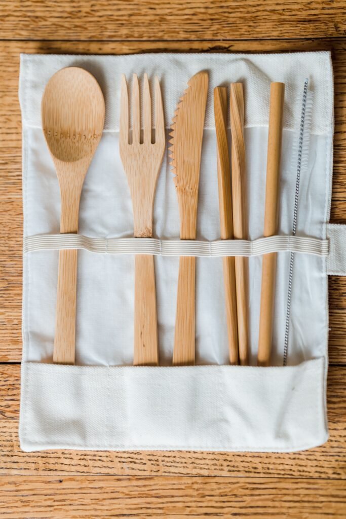 A set of sustainable bamboo utensils in a fabric holder on a wooden table, promoting zero waste.